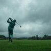 雨のゴルフコースで緑色のレインウェアを着てスイングする男性ゴルファー